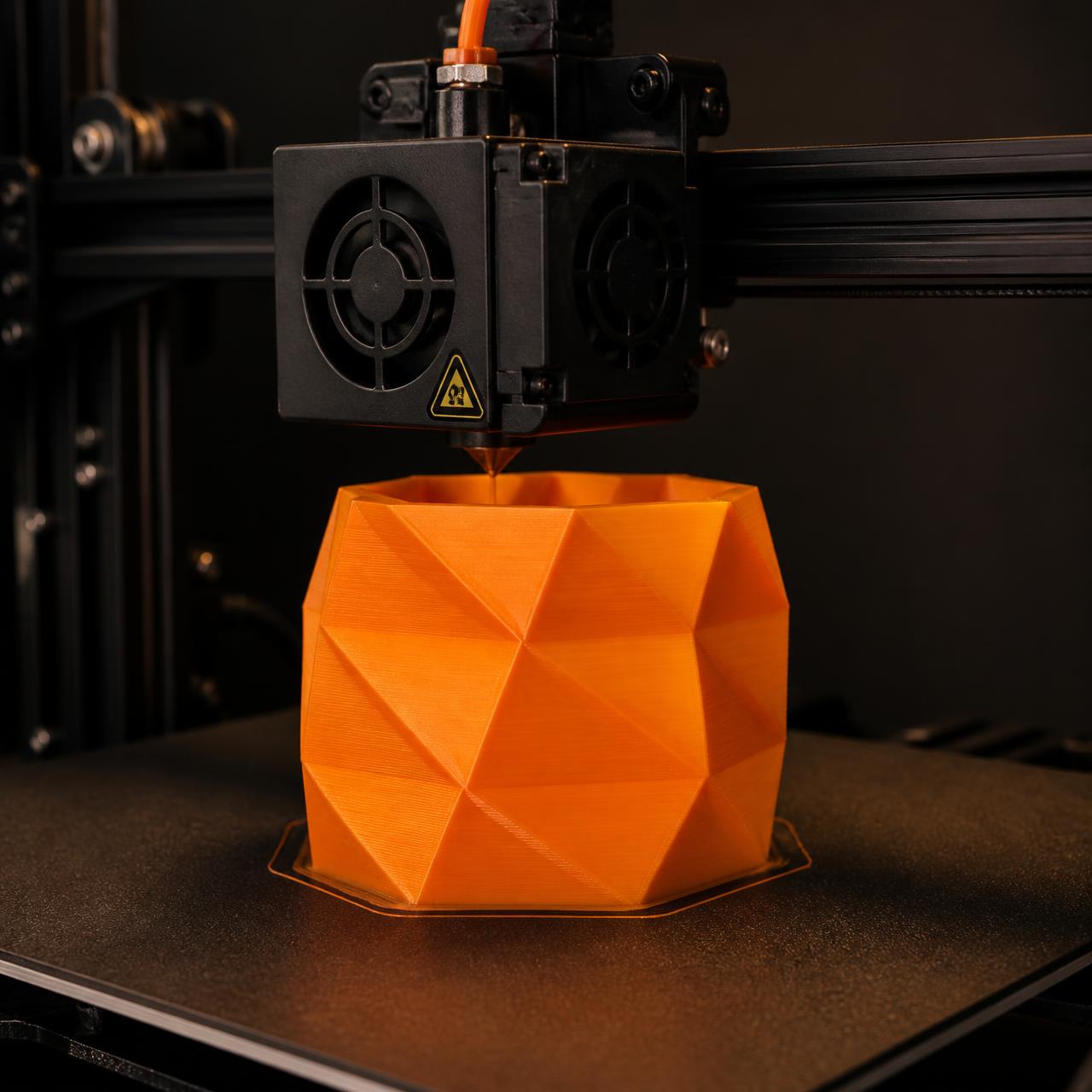 Impressora 3D produzindo uma peça geométrica laranja